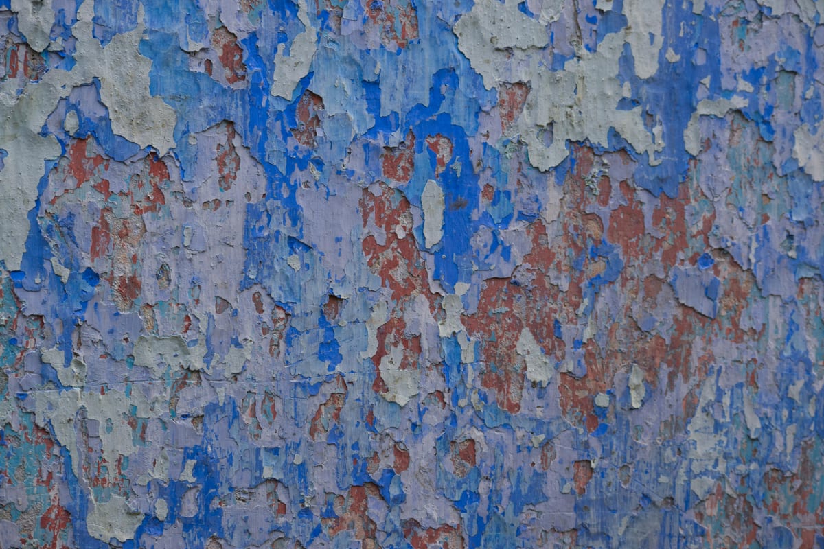 A wall of peeling paint — blue, grey, rust — built up in layers over time.