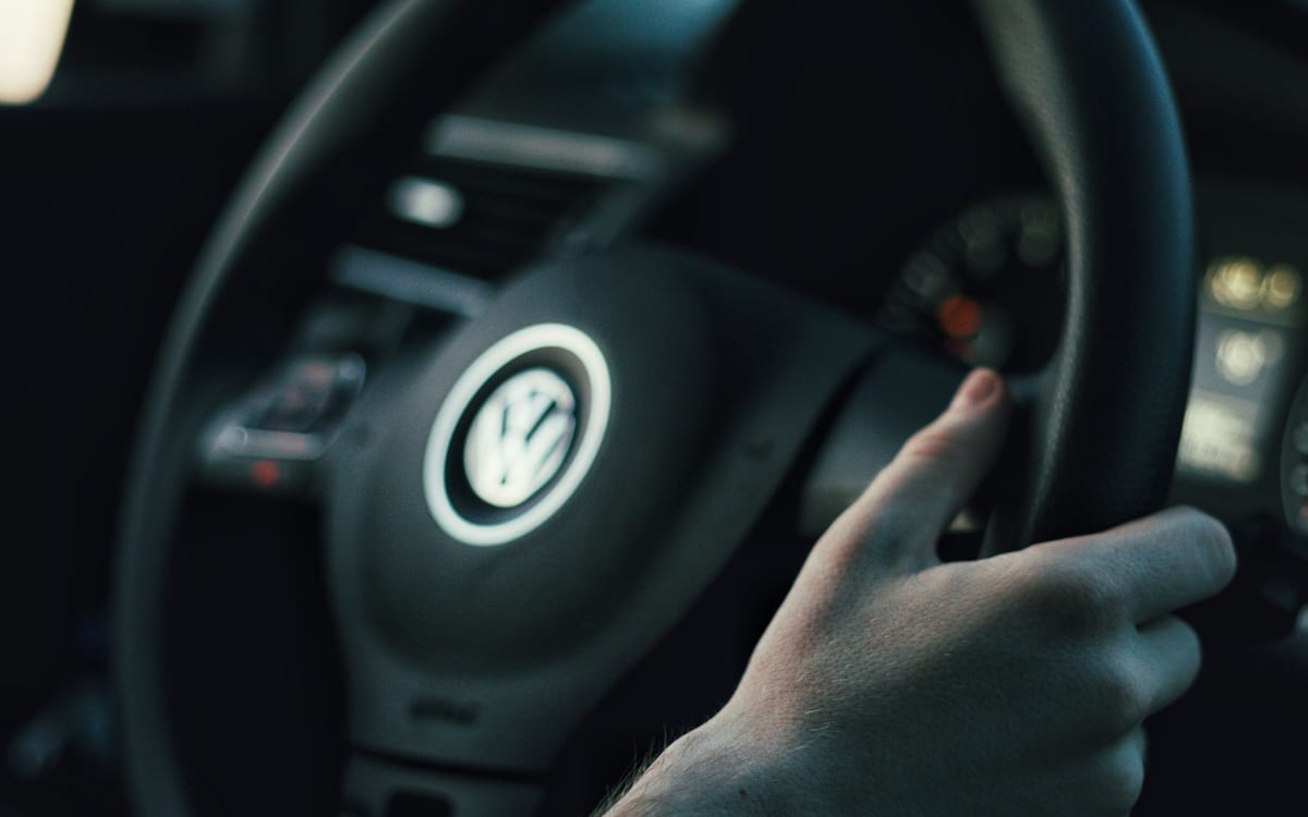 Una mano stringe il volante di un'automobile in penombra, il quadrante sfocato sullo sfondo. Chi tiene il volante decide la traiettoria; il contratto decide chi paga l'arrivo.