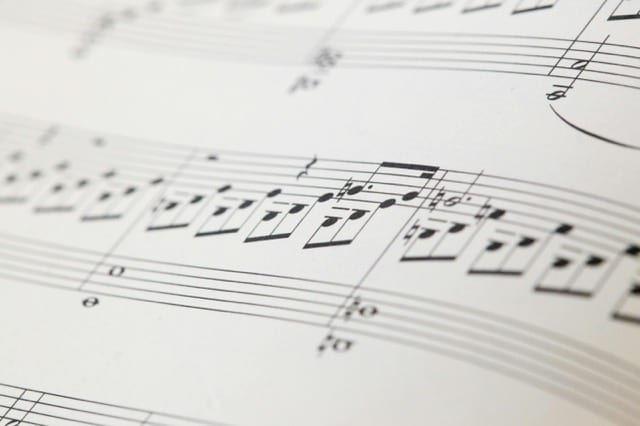 A close-up of a musical score, black notes lined up on the staves, the staff itself a strict grid that makes composition possible. Constraint as shape.